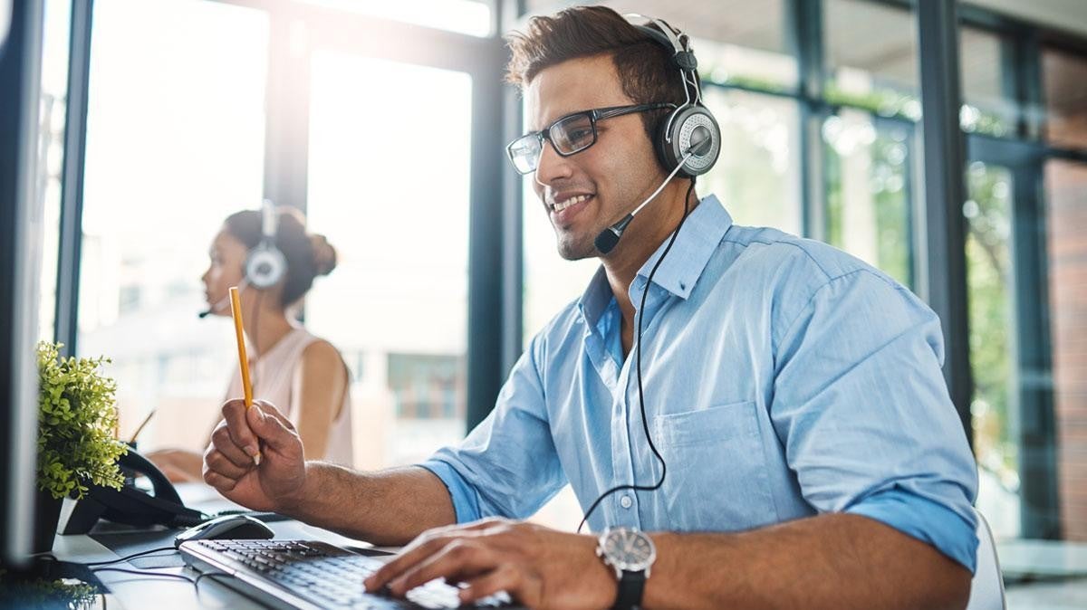 Man with headset smiling while working on a computer in a modern office