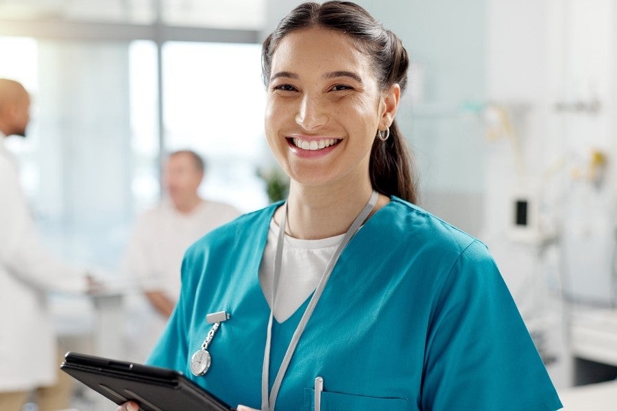 Smiling nurse holding a tablet in a hospital setting.