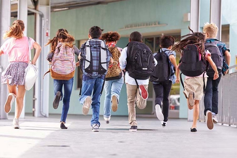 Group of kids with backpacks running toward a school building.
